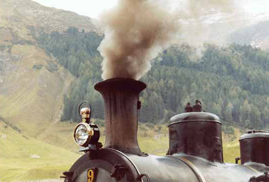 Bild 5 Nahaufnahme Lampe, qualmender Schornstein mit Dom und Pfeife Hintergrund bewaldeter Berg